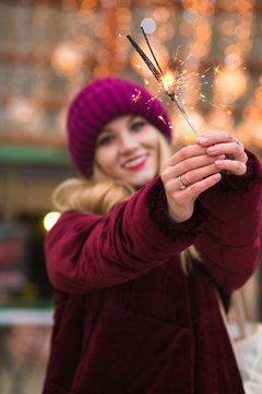 Stunning blonde girl holding glowing Bengal lights at the Christmas fair in Kiev. Blur effect