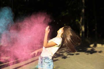 Joyful young woman with wind in hair playing with blue and pink dry paint Holi