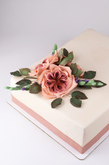 Rectangular art cake decorated with pink flowers and green leaves from mastic on a white wooden table. Picture for a menu or a confectionery catalog.