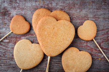 Ginger cookies on a stick in the form of hearts are piled in a heap on a wooden table