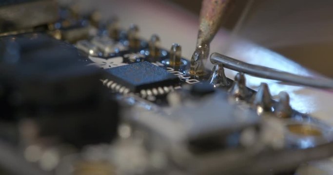 Detail of soldering an electrical connection with a hot soldering iron bit and solder, looking across small circuit board. Macro shot recorded in 4K, slow motion at 60fps.