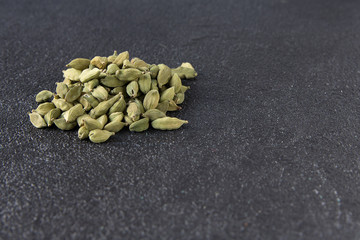 Green cardamom pods on a black stone background.