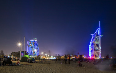 Naklejka premium People waiting for new year celebration at the beach in last day of the year. The world's first seven stars luxury hotel Burj Al Arab and Dubai Marina in background 
