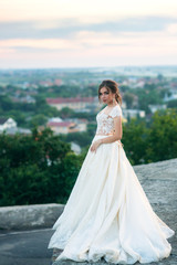 Fototapeta na wymiar Young girl in wedding dress on city background at sunset. Summer