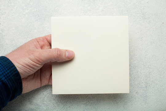 A square cream layout of a sheet of paper in hand.