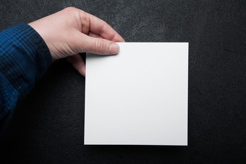 Blank white square sheet of paper in hand on a black background.