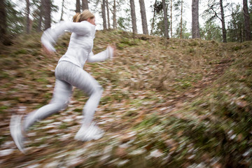 Motion blurred photo of woman running in woods in cold weather