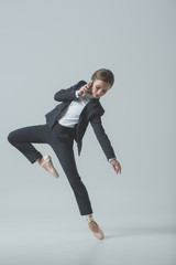 businesswoman in suit and ballet shoes dancing and talking on smartphone, isolated on grey