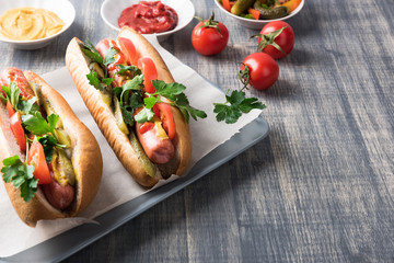 Hot dogs on wooden background. Homemade sandwiches with sausages, tomatos, pickles, mustard and ketchup on plate. Wrapping paper