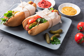 Hot dogs on wooden background. Homemade sandwiches with sausages, tomatos, pickles, mustard and ketchup on plate. Wrapping paper