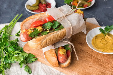 Hot dogs on wooden background. Homemade sandwiches with sausages, tomatos, pickles, mustard and ketchup on plate. Wrapping paper