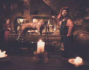 Medieval man doing roasted pig on the rack in ancient castle kitchen