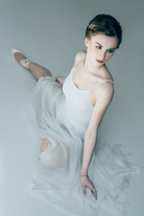 Obraz premium attractive ballerina sitting in white dress and ballet shoes