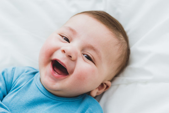Portrait of an adorable 3 month old baby smiling lying in a bed of white sheets