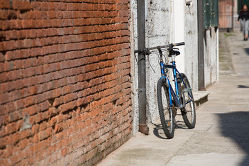 An old bicycle stands near the brick wall of the house