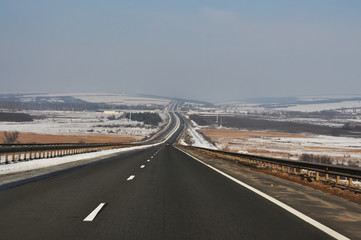 The road is going off into the distance among the winter fields and hills. Endless expanse.
