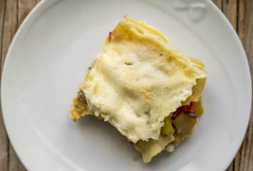 Piece of homemade roasted vegetarian lasagna on the white plate on the wooden table