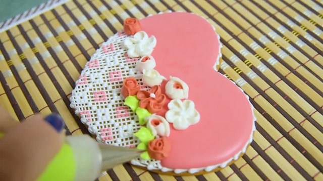 woman confectioner decorates and decorates the glaze with gingerbread cookies in the shape of heart. Valentine's Day, February 14, symbol, valentine, gift.