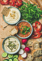 Vegan snack board. Flat-lay of various Vegetarian dips hummus, babaganush and muhammara with crackers, bread and fresh vegetables, top view. Clean eating, healthy, dieting food concept.