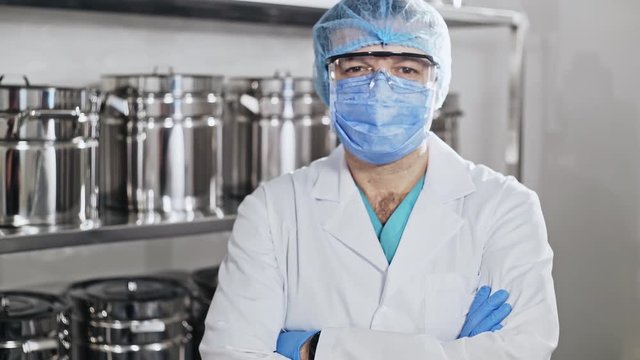 Portrait of a healthcare worker in a mask and protective glasses against the background of a rack with metal utensils.