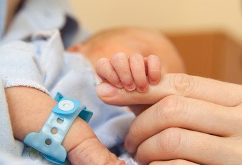 The baby clings to his mother's finger - obrazy, fototapety, plakaty