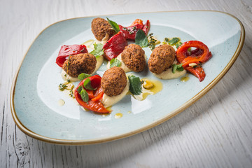 Hummus with falafel medallions in plate on white rustic wooden table