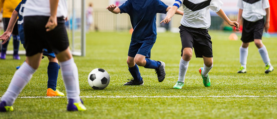 Obraz premium Kids kicking soccer match. Boys playing soccer tournament game on pitch. Goalkeeper standing in goal in the background