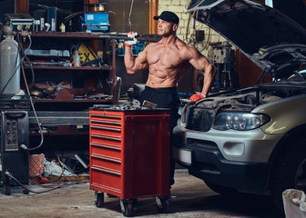 Shirtless mechanic in a garage.