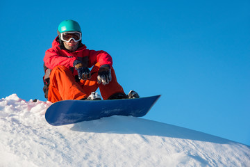 Fototapeta na wymiar Low angle shot of a male snowboarder sitting on top of the mountain enjoying warm sunny winter day outdoors copyspace resort recreation active lifestyle seasonal sports