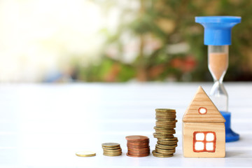 time to pay/ wooden house next to a pile of coins and an hourglass