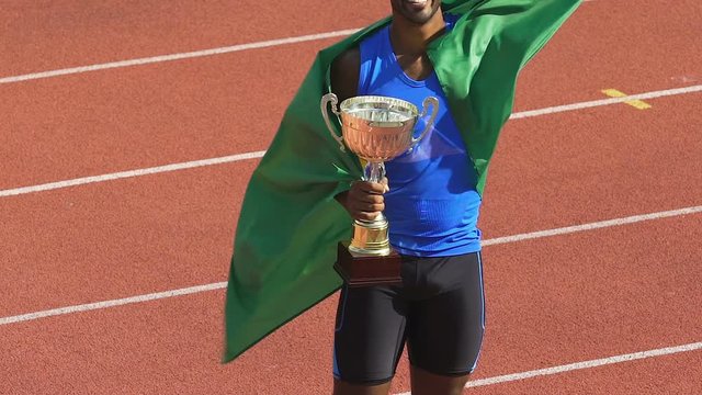 Athlete wrapped in his country flag victoriously holding deserved cup, triumph