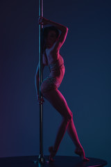 side view of beautiful sensual female dancer posing with pole on blue