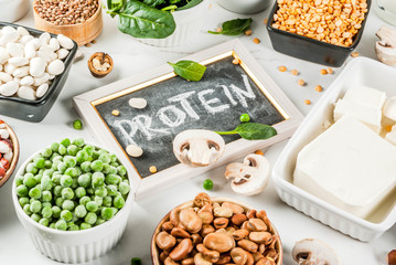 Healthy diet vegan food, veggie protein sources: Tofu, vegan milk, beans, lentils, nuts, soy milk, spinach and seeds. Top view on white table.