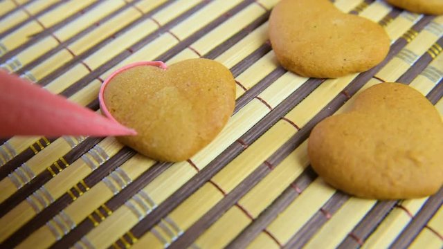 the woman decorates the confectioner and decorates the croquet with the glaze on the Valentine's Day. The inscription love on home cookies is handmade.