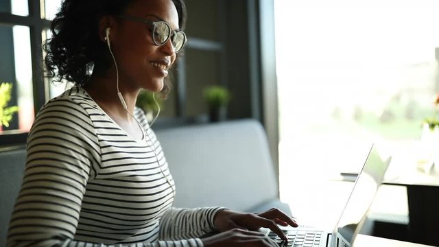 Smiling African woman wearing earphones and working on a laptop