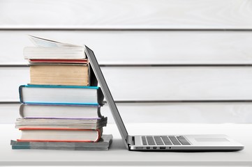 Stack of books with laptop on wooden table
