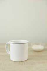 Fototapeta na wymiar ENAMEL COFFEE MUG Enamel white coffee mug and small transparent milk bowl on a wood table.