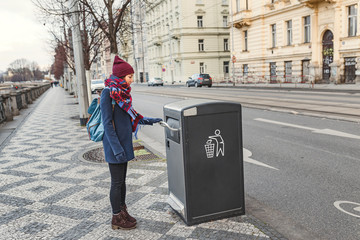 Portrait of a young woman throwing garbage in recycling bin at city street