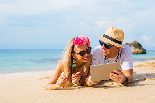 Couple relaxing on the beach and looking at tablet computer