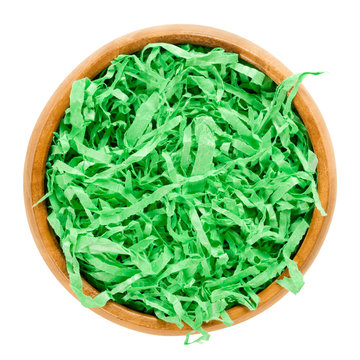 Green paper Easter grass in wooden bowl forming a nest. Vibrant colored and crinkled gift basket shred for filling and decoration. Isolated macro food photo close up from above on white background.