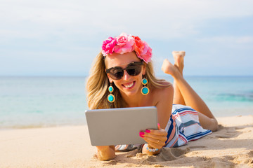 Cheerful young woman lying on the beach in sand and using tablet