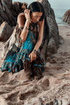 boho styled young hippie girl sitting on beach at sunset