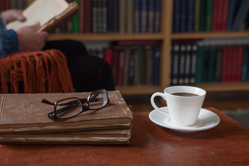 Sweet moments of relaxation with books and a cup of coffee. Vintage books, glasses, chair, library, man