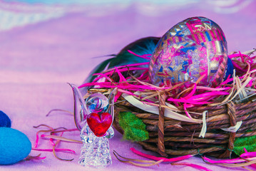 Decorative Easter egg, glass angel with heart and woolen eggs in the busket on the purple background
