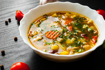 Bowl of chicken soup with noodle and vegetables on a dark wooden background.