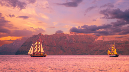 Sailboat in Santorini, Greece. Sailing ship navigate near an island in Cyclades. The photo is taken at sunset. - obrazy, fototapety, plakaty