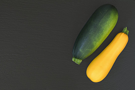 Fresh green zucchini and yellow zucchini on a black stone surface.  Top view, copy space. Healthy eating concept.