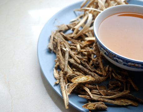 Bowl Of Chinese Herb Tea With Dried Assorted Roots Aside.