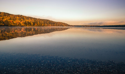 Wilderness Lake Reflections. Monocle Lake in northern Michigan with autumn foliage reflected in the calm blue water of the lake and a sunset horizon. Hiawatha National Forest, Brimley, Michigan.