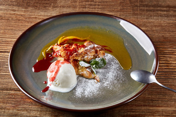 Apple strudel with mint and ball of vanilla ice cream on dish on a wooden background. All sprinkled with powdered sugar.